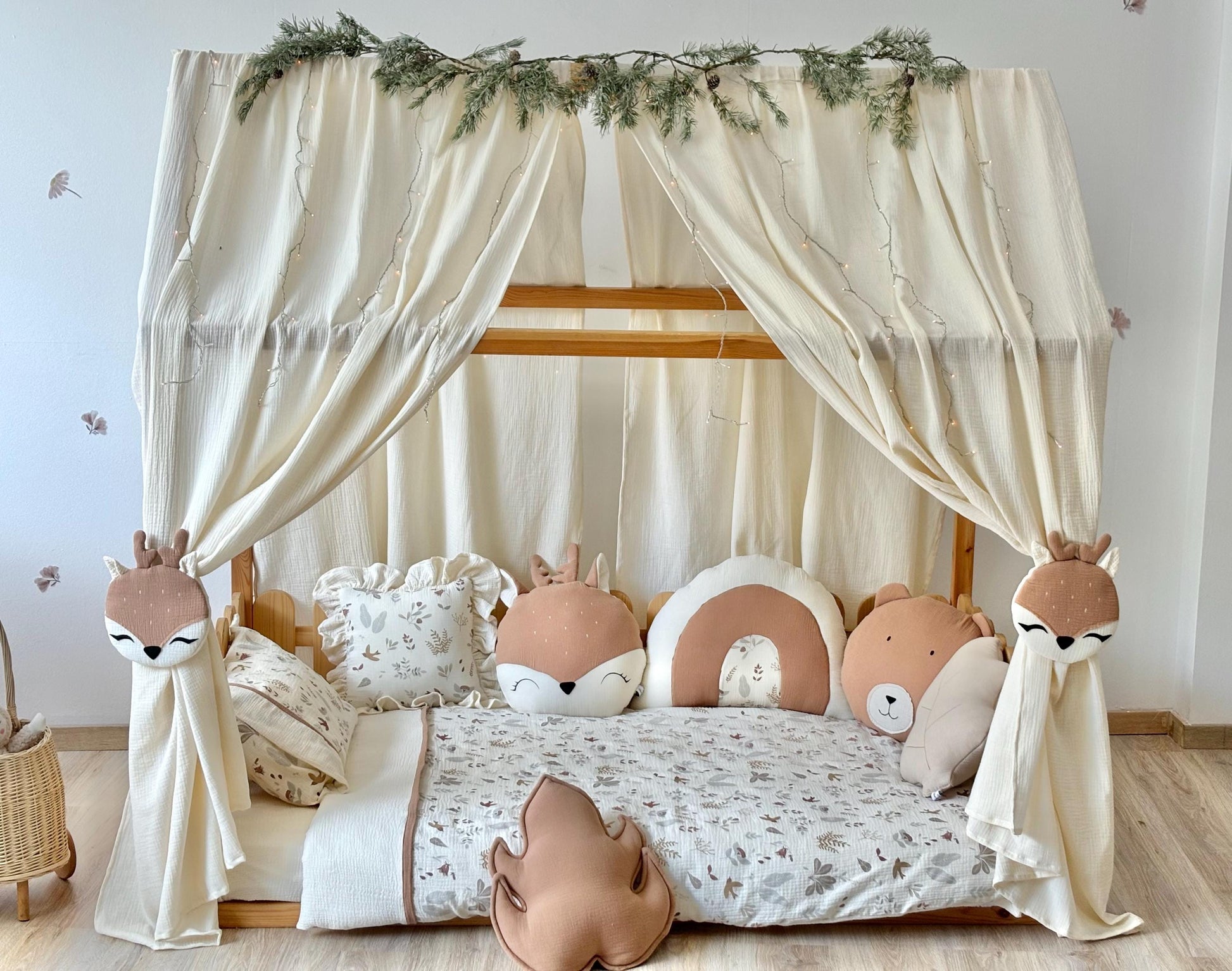 Neutral playroom setup with muslin canopy, wooden bed frame and cuddly stuffed animals.
