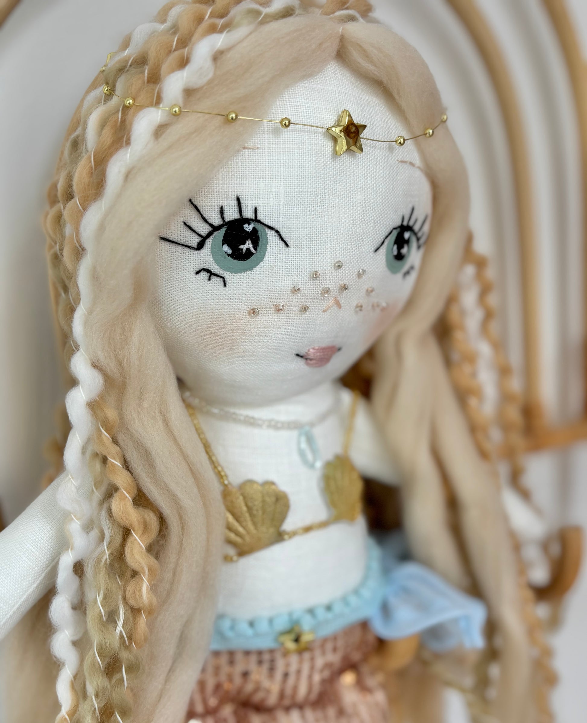 Handmade mermaid doll with hand-stitched face, yarn hair and soft fabric tail, styled in a neutral beach-inspired setting